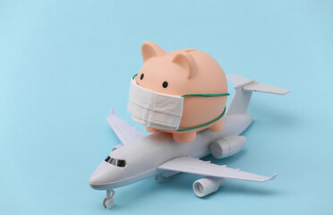 Wall Mural - Piggy bank in a medical mask with a passenger plane figure on a blue background. Travel during the pandemic covid-19