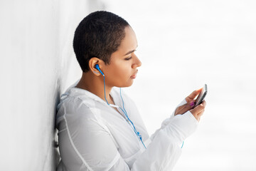 Sticker - fitness, sport and technology concept - young african american woman with earphones listening to music on smartphone outdoors