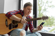 © Syda Productions - leisure, music and people concept - young man or musician playing guitar sitting on windowsill