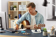 © Syda Productions - leisure and people concept - young man or musician with guitar sitting at table and writing to music book at home