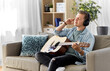 © Syda Productions - leisure, music and people concept - young man or musician in headphones playing guitar sitting on sofa at home