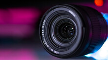 The Camera Lens Is Illuminated With Neon Light. Close-up. Dark Neon Background.