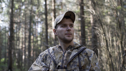 Portrait of handsome young man hunter or tourist. Man in camouflage clothes hunts outdoor in forest hunting alone. Close up of man hiker standing in forest. Hunter searching animal tracks.