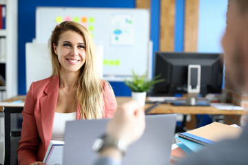 A beautiful female employee is sitting in the office in front of her boss and smiling. Woman putting pressure on the man sitting in front of her