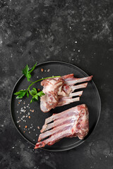 Wall Mural - Raw ribs of a young lamb. Raw lamb ribs in a black ceramic plate on the black kitchen table. Raw meat of a young lamb on the table