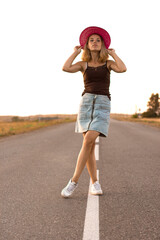 a young girl stands on the road at the dividing strip in a pink hat and white sneakers, sunset soldier, street