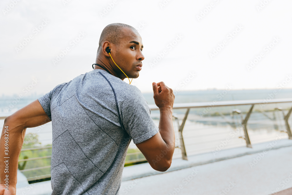 Side view of a young african man jogger exercising outdoors - obrazy, fototapety, plakaty 
