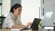 © Prathankarnpap - A beautiful woman is using a computer tablet with a keyboard case while sitting at the wooden table.