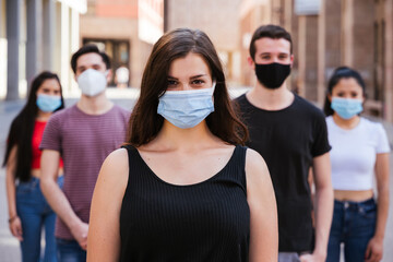 Portrait of a multiracial group of friends with masks in protection from Coronavirus infections, Covid-19 - Leader woman with other millennials behind her with serious eyes looking into the camera