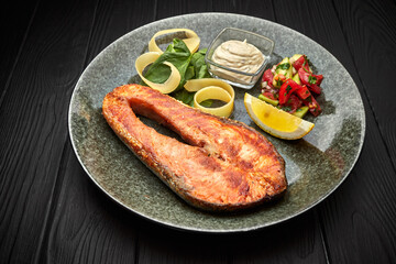 Wall Mural - Salmon steak with vegetables, lemon and sauce, on a black wooden background