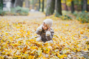 Little girl having fun in dry leaves on a beautiful autumn day.