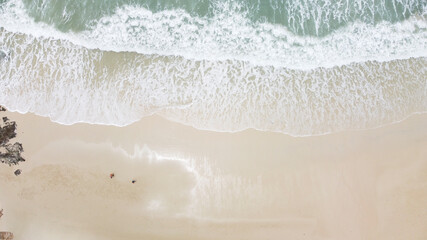 View from above, stunning aerial view of a person walking on a beautiful beach bathed by a turquoise sea during sunset.