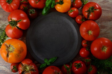 Colorful organic tomatoes - red tomatoes and yellow tomatoes around an empty clay plate. Tomatoes background. Copy space and text area