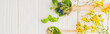 panoramic shot of herbs and green leaves in spoons near flowers on white wooden background, naturopathy concept