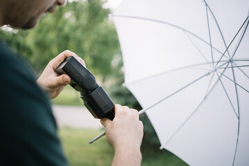 Canvas Print - Cropped man connecting flash to light stand in nature. Close-up view of photographer setting flash to light stand with umbrella while standing in forest.