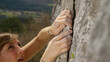 © helivideo - CLOSE UP: Fit female lead climber holds on to a flake grip on a massive cliff.
