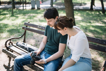 Wall Mural - Female model and male photographer checking photos on camera. Man holding camera while sitting on bench next to girl and checking images.