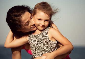 happy beautiful mother hugging and kissing her playful enjoying kid girl on vacation sea summer holi