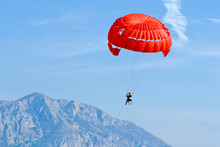 Tandem, Two Persons Flying On A Red Parachute On Sky Background