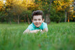 © Dragosh - A smiling young boy lying on the green grass, enjoys the park, looks at the camera on a sunny summer day.