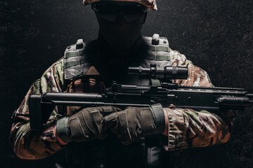 Soldier in multi camouflage uniform and  military armored vest holding sniper rifle.