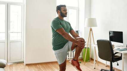 Start your day with fitness. Young active man looking away, stretching his legs during morning workout at home