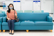 © DG PhotoStock - Asian woman with hygiene protective face mask over her face sitting on a sofa seat in the hospital with a social distancing protocol while COVID-19 or Coronavirus outbreak. Using face mask concept.