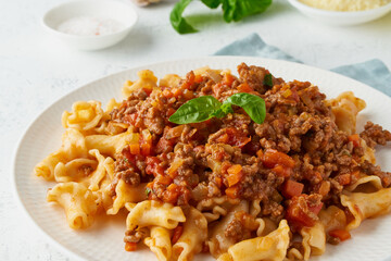 Wall Mural - Pasta Bolognese campanelle with mincemeat and tomato sauce, parmesan cheese, basil. Italian dinner, white table. , side view, close up