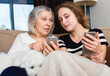 © JackF - Young and aged women sitting together on sofa and using mobile gadgets