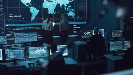 Poster - Two Software Engineers Talking Next to a Big Screen in a Modern Monitoring Office with Live Analysis Feed with Charts. Monitoring Room Big Data Scientists and Managers Sit in Front of Computers.