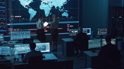 Poster - Two Software Engineers Talking Next to a Big Screen in a Modern Monitoring Office with Live Analysis Feed with Charts. Monitoring Room Big Data Scientists and Managers Sit in Front of Computers.
