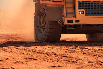 Large mining dump truck lifts orange dust on wheels
