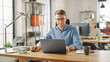 © Gorodenkoff - Handsome Young Man in Glasses and Shirt is Working on a Laptop in a Creative Business Agency. They Work in Loft Office. Diverse People Working in the Background. He's in Good Mood.