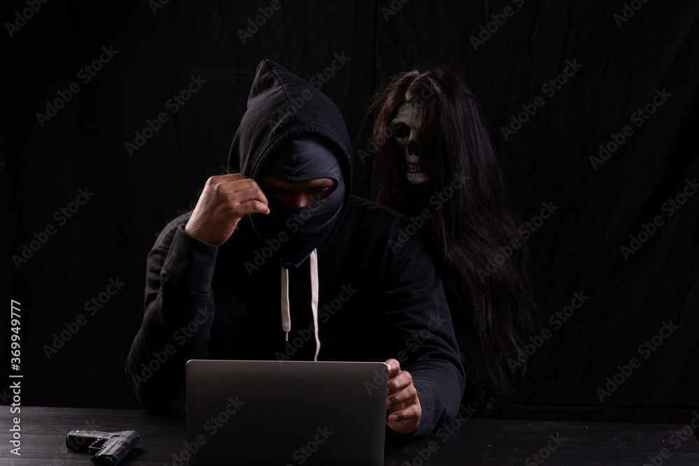 Mysterious man in the hood with skull inside using laptop on table with ...