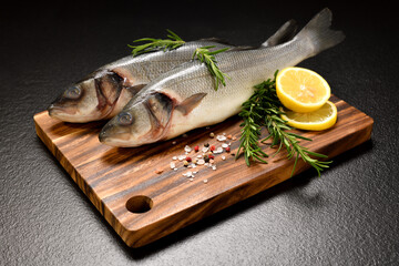 Wall Mural - Fresh seafood Sea Bass fish arranged on black stone background