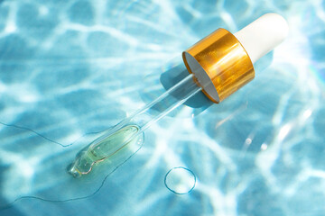 Cosmetic pipette on a blue background with water shadows, underwater effect. Stylish concept of organic essences, sea health products. Copy space, minimalism, flat lay. Marine cosmetics.