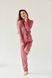 © standret - Cheerful young woman in pajamas standing indoors against white background in the studio