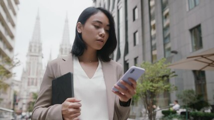 Young attractive asian woman wearing formal suit using mobile phone typing text messages walking outside business cellphone city smartphone slow motion