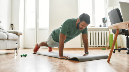 Online workout. Male fitness instructor showing push up exercises while streaming, broadcasting video lesson on training at home using laptop. Sport, online gym concept