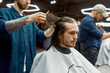 © Svitlana - Working process. Young hipster guy sitting in barbershop chair and getting new trendy haircut. Professional barber serving client
