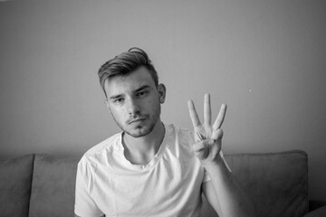 Black and White, Young man wearing a t-shirt with counting hand signs sitting in a isolated green background, showing number three