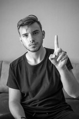 Black and White, Young man wearing a t-shirt with counting hand signs sitting in a isolated green background, showing number one