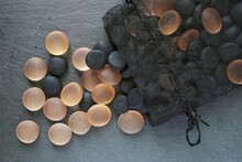 Black And Orange Stones In A Transparent Black Bag And Scattered Alongside On The Gray Slate Surface