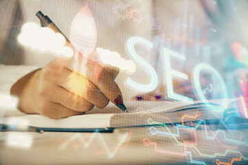 Double exposure of woman's hands making notes with SEO icon. Concept of Search engine optimization