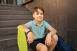 School Boy in blue polo shirt sitting on the stairs with a blue backpack and green penny board