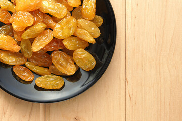 Large yellow and sweet raisins on a black plate that stands on a wooden table