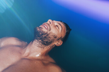 Wall Mural - Handsome beard man floating in tank filled with dense salt water used in meditation, therapy, and alternative medicine.