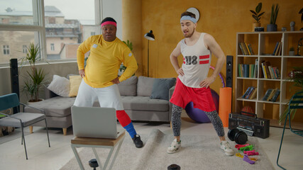 Joyful and funny retro style unfit sportsmen doing fun sports routine dancing with exercises into music during home training. Multi-ethnic fitness team.