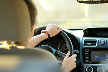 Canvas Print - Close up view of woman holding steering wheel driving a car on city street on sunny day.