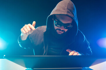 Poster - A bearded man with black glasses gestures next to a laptop. Working on a computer. Computer gadgets. Hacker. An emotional man is typing on a computer.
